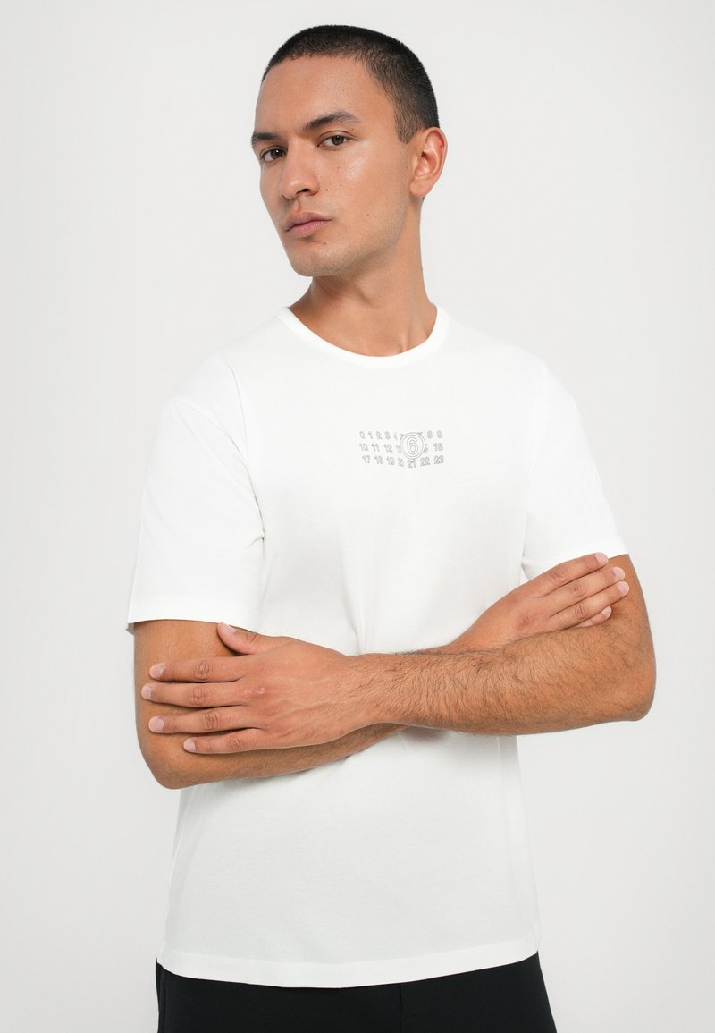 T-shirt bianco in cotone con stampa grafica con numeri sul petto, maniche corte e scollatura a girocollo. Vestibilità standard.