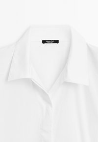 Hvid skjorte med krave lavet af bomuld. Har et klassisk design med en ren halsudskæring og subtil tekstur. Etiketten med "Massimo Dutti" er synlig.