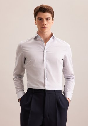 Chemise boutonnée bleu clair avec un motif à carreaux subtil, manches longues et col classique, assortie à un pantalon sombre.