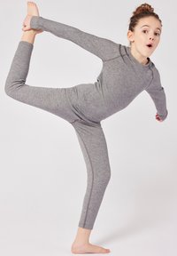 Body atletico grigio a maniche lunghe con gambe aderenti, texture liscia e dettagli delle cuciture in contrasto. Il modello esegue una posa di yoga.
