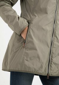 Warm, olive green jacket with a shiny, smooth texture, featuring a zippered front and side pockets. Includes metallic hardware accents.
