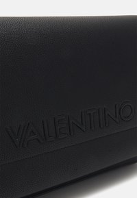 Czarna skórzana kopertówka o teksturowanym wykończeniu, z wytłoczonym logo „VALENTINO” z przodu, prostokątny kształt i elegancki design.