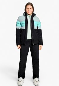 Padded jacket with a black base and light teal horizontal stripes; features a hood, front zipper, and a fitted silhouette. Black snow pants below.