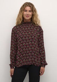 Bluza dugih rukava od tamnosmeđeg platna s cvjetnim uzorkom u ružičastoj i krem boji. Visoki ovratnik s nabranim detaljima i dugmadima na manžetama.