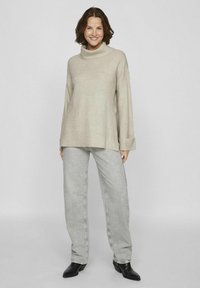 Pull à col roulé beige avec une coupe décontractée et des poignets à côtes, associé à un jean gris clair à jambes larges et des bottines noires.