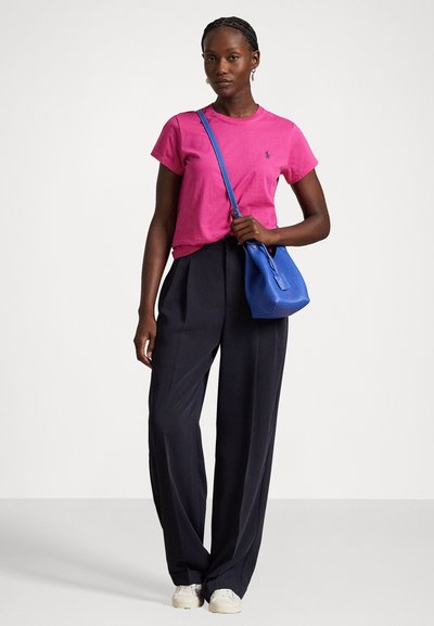 Rosa Baumwoll-T-Shirt, entspannte Passform, marineblaue weite Hosen, blauer Crossbody-Bag, weiße Sneakers. Schlichte Texturen mit minimalen Details.