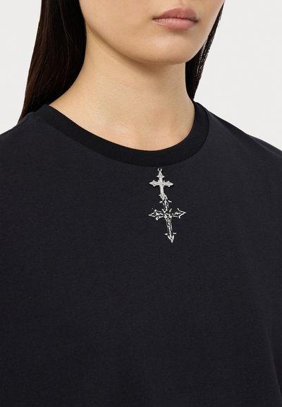 Sort bomulds T-shirt med rund hals og sølv broderi af et kors på brystet. Glat tekstur og afslappet pasform.