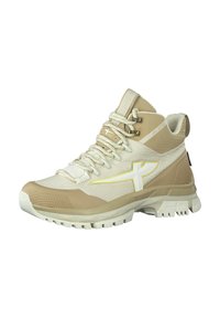 Scarpa da trekking alta beige e crema con tessuto testurizzato, suola in gomma, logo giallo prominente e occhielli in metallo per i lacci.
