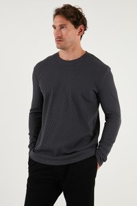Cămașă lungă cu mâneci gri, realizată dintr-un material ribbed, având un guler rotund și o croială lejeră. Asortată cu pantaloni negri, design minimalist.