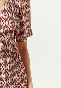 Kortärmad klänning i lättviktsmaterial med ett upprepande geometriskt mönster i rosa, grönt och krämfärg med volang vid halsringningen.