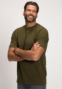 T-shirt verde oliva in cotone, colletto rotondo, maniche corte, con un logo sottile sul petto. Tessuto liscio, vestibilità rilassata.