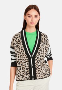 Karobe im Leopardenmuster mit schwarz-weißen gestreiften Ärmeln, ausgestattet mit einem V-Ausschnitt, sechs Knöpfen und einem kontrastierenden grünen Hemd darunter.