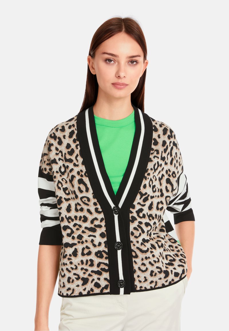 Karobe im Leopardenmuster mit schwarz-weißen gestreiften Ärmeln, ausgestattet mit einem V-Ausschnitt, sechs Knöpfen und einem kontrastierenden grünen Hemd darunter.