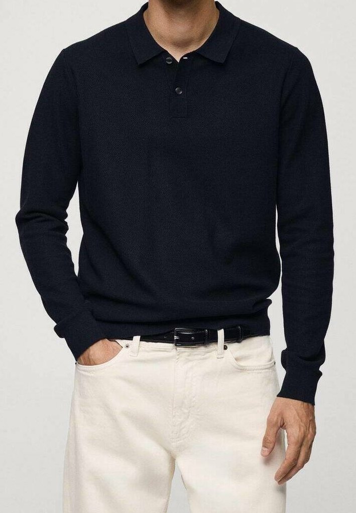 Polo à manches longues bleu marine avec une finition texturée, patte de boutonnage et col. Assorti avec un pantalon blanc et une ceinture noire.