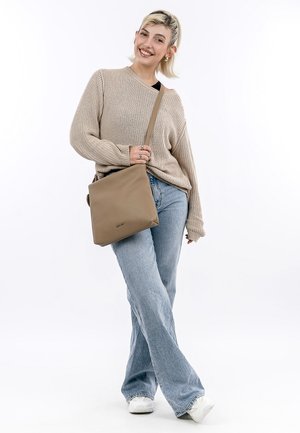Brown leather crossbody bag with a textured finish, square shape, and a long strap, paired with a tan knit sweater and faded blue jeans.