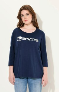 T-shirt bleu marine avec un col rond et des manches trois-quarts. Présente le texte argenté "Queens" imprimé sur le devant.