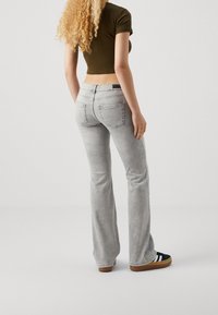 Jean gris évasé en denim, avec une taille mi-haute et des poches arrière. Associé à un haut sombre et des chaussures à enfiler à rayures noires.