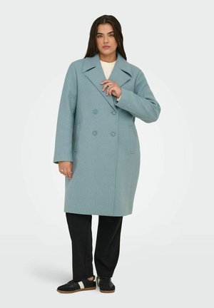 Helleblaue Wollmischung-Jacke mit doppelreihigem Design, großen Revers und zwei Knopfverschlüssen, kombiniert mit schwarzen Hosen und schwarzen Sneakers.