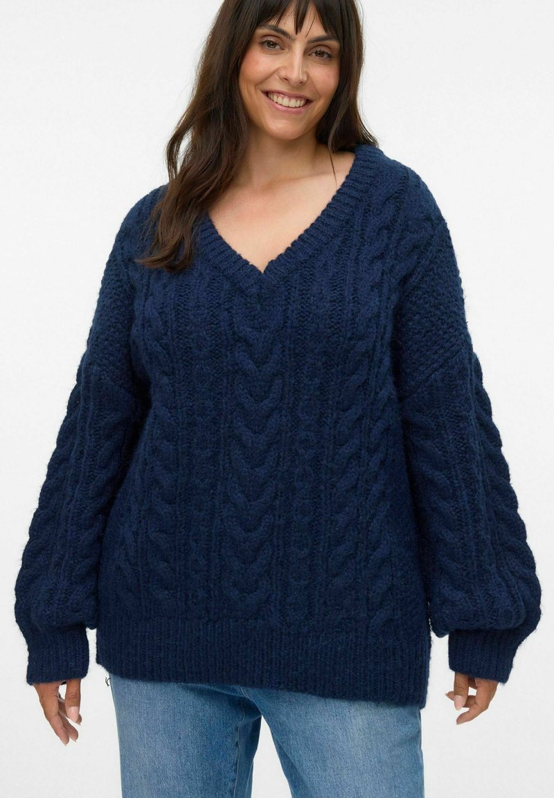Pull en maille bleu marine avec un col en V, présentant des motifs en câble et des manches surdimensionnées. Fabriqué en fil texturé pour la chaleur.