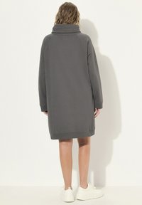 Graues Sweatshirtkleid mit hohem Kragen, langen Ärmeln und gerippten Bündchen, das eine lässige Passform und glatte Textur aufweist. Getragen mit weißen Sneakern.