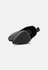Black ankle boot with a pointed toe and a textured rubber sole. The exterior features a smooth leather finish and a small pull tab.