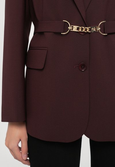 Burgundy blazer with a structured design, featuring a gold chain belt buckle and front pockets. Smooth fabric with a matte finish.