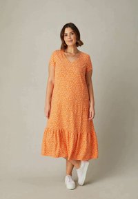 Orangenes, blumengemustertes Midikleid mit V-Ausschnitt, kurzen Ärmeln und einem Rüschensaum. Kombiniert mit weißen Sneakern für einen lässigen Look.