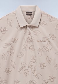 Beige polotröja med ett subtilt bladmönster, med klassisk krage och placket med tre knappar. Logotyp broderad i matchande färg.