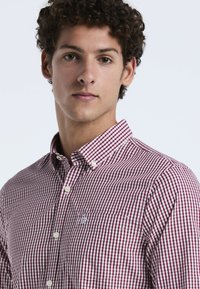 Rood en wit geruit button-up shirt met een puntige kraag en borstzak, gemaakt van een gladde stof met witte knopen.