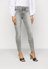 Jeans skinny em denim cinza claro com uma bainha desfiada, combinados com mules de salto aberto pretos. Design simples e ajustado.