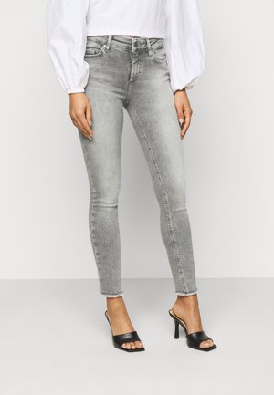Jeans skinny em denim cinza claro com uma bainha desfiada, combinados com mules de salto aberto pretos. Design simples e ajustado.