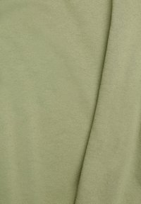 Gros plan d’un tissu vert clair à texture fine en maille avec des plis doux sur le côté droit.