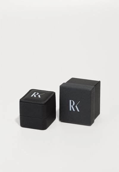 Schwarze Verpackungsboxen mit einer strukturierten Oberfläche; eine Box hat eine quadratische Form mit einem gepolsterten Deckel, beide verfügen über ein silbernes "RK"-Logo.