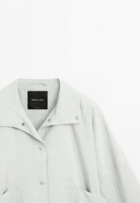 Jasnoszara kurtka z zatrzaskami, szerokim kołnierzem i dwoma przednimi kieszeniami, oznaczona marką Massimo Dutti, położona na płasko na białym tle.