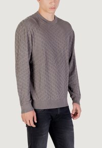 Pull en tricot gris avec un motif texturé, encolure ronde et poignets côtelés. Le tissu présente un design doux et légèrement surélevé.
