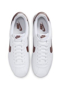 White sneakers with a smooth leather upper, brown accents on the swoosh and heel, and a white laced closure. Textured interior lining.