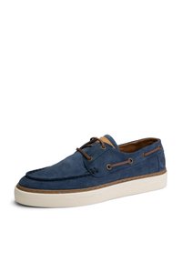 Zapato de barco de ante azul marino con cordones marrones, detalles de cuero y suela de goma blanca. Parte superior perforada para añadir textura.
