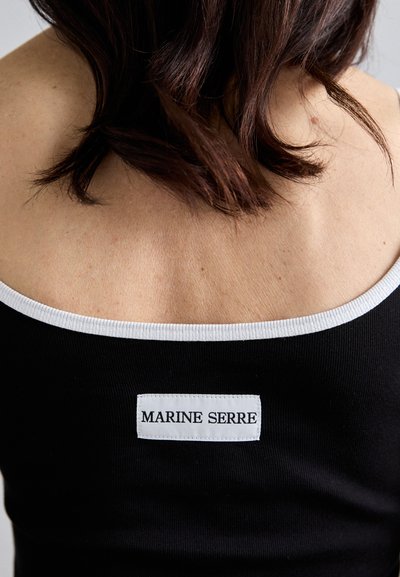Črn pleten top brez rokavov z belim obrobo okoli izreza in belim napisom "MARINE SERRE" na hrbtu.