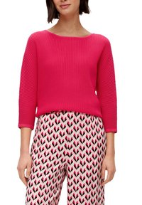 Fuchsie-gestreifter Pullover mit weitem Ausschnitt und Dreiviertelärmeln, kombiniert mit gemusterten Hosen mit pinken und schwarzen Zickzackmustern.