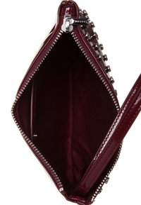 Burgundowa lakierowana kopertówka z metalowymi elementami w kolorze srebrnym, zamknięcie na suwak i gładkie wnętrze. Posiada ćwiekowane akcenty z jednej strony.