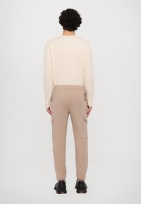 Beige langermet skjorte og lysebrune cargo-bukser med lommer; avslappet passform med elastisk midjebånd; brukt med svarte joggesko.