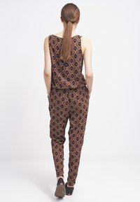 Ensemble deux pièces comprenant un haut sans manches et un pantalon fuselé, tous deux ornés d'un motif de diamants multicolores sur un fond sombre.