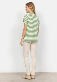 Grøn- og hvidstribet t-shirt med kort ærme, løs pasform og sideudskæringer, paired med beige stramme bukser og lysebrune flade sko.