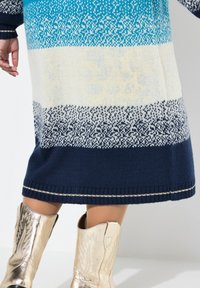Strickkleid mit Ombre-Muster in Blau, Creme und Marine. Verfügt über gerippte Bündchen und Saum mit metallischen Akzentstichen.