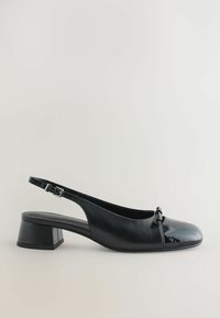 Svart slingback-sko med en glänsande lacktå och en matt läderkropp. Har en liten rosettdetalj och en fyrkantig klack.