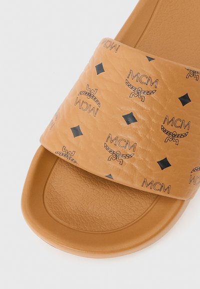 Sandale tongs beige avec une semelle texturée et une large bride ornée de logos MCM noirs et de motifs en forme de diamants.