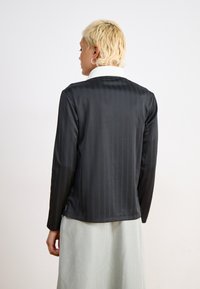 Μαύρο πουκάμισο με μακριά μανίκια και κατακόρυφες ρίγες, με λευκό γιακά. Λείο ύφασμα, άνετη γραμμή και ίσια τελείωση στη μέση.