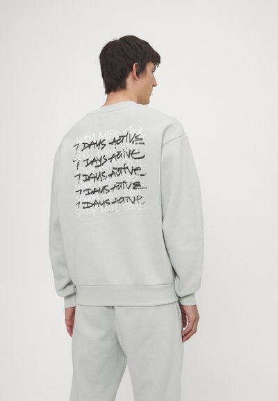 Light gray sweatshirt with long sleeves and ribbed cuffs. Features large graphic text on the back, "7 DAYS ACTIVE," in black and white.