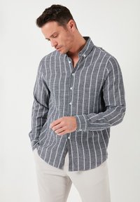 Camisa de manga larga abotonada en tela gris con rayas verticales blancas. Presenta un cuello clásico y puños con un botón.