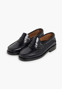 Mocasines de cuero azul marino con un acabado brillante, que presentan punta cosida, detalles de pespunte y un tacón bajo. Forro interior marrón.